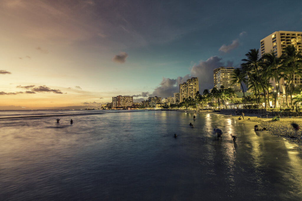 Night Panorama Of Waikiki Beach And Building By The Shore Line With Palm Trees In Honolulu