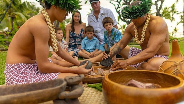 Kona's Feast & Fire Luau: a family watches as Polynesian men pound poi